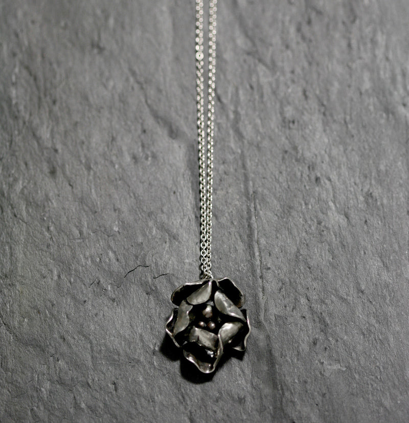 A Sterling silver hand carved flower necklace with two layers of individually textured and shaped rose petals. Treated with gentle oxidation techniques and re-polished making every piece unique. On an 18 inch fine silver chain with a handmade catch.