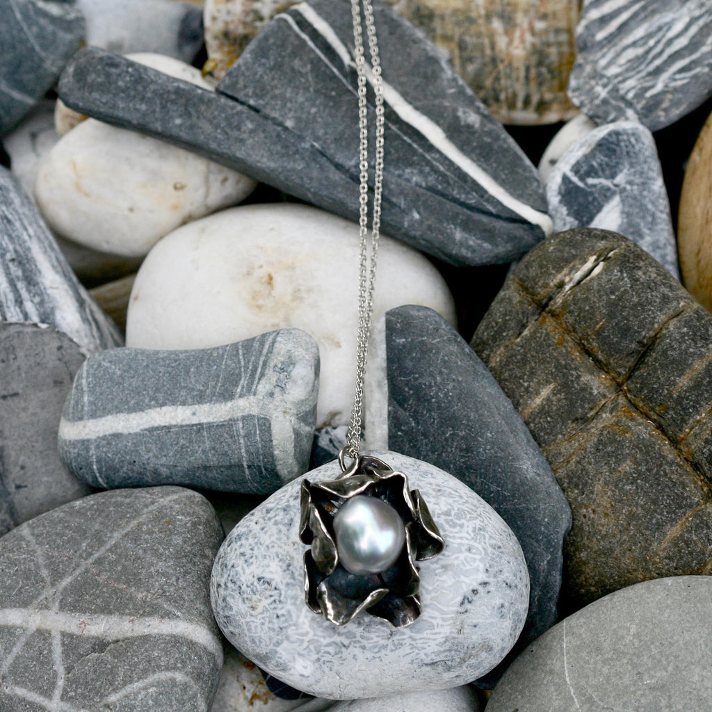 Hand carved Sterling silver rose necklace with two layers of individually shaped rose petals, gently oxidised before a baroque pearl is carefully set and re-polished. On an 18 inch Silver trace chain with a handmade hook catch.