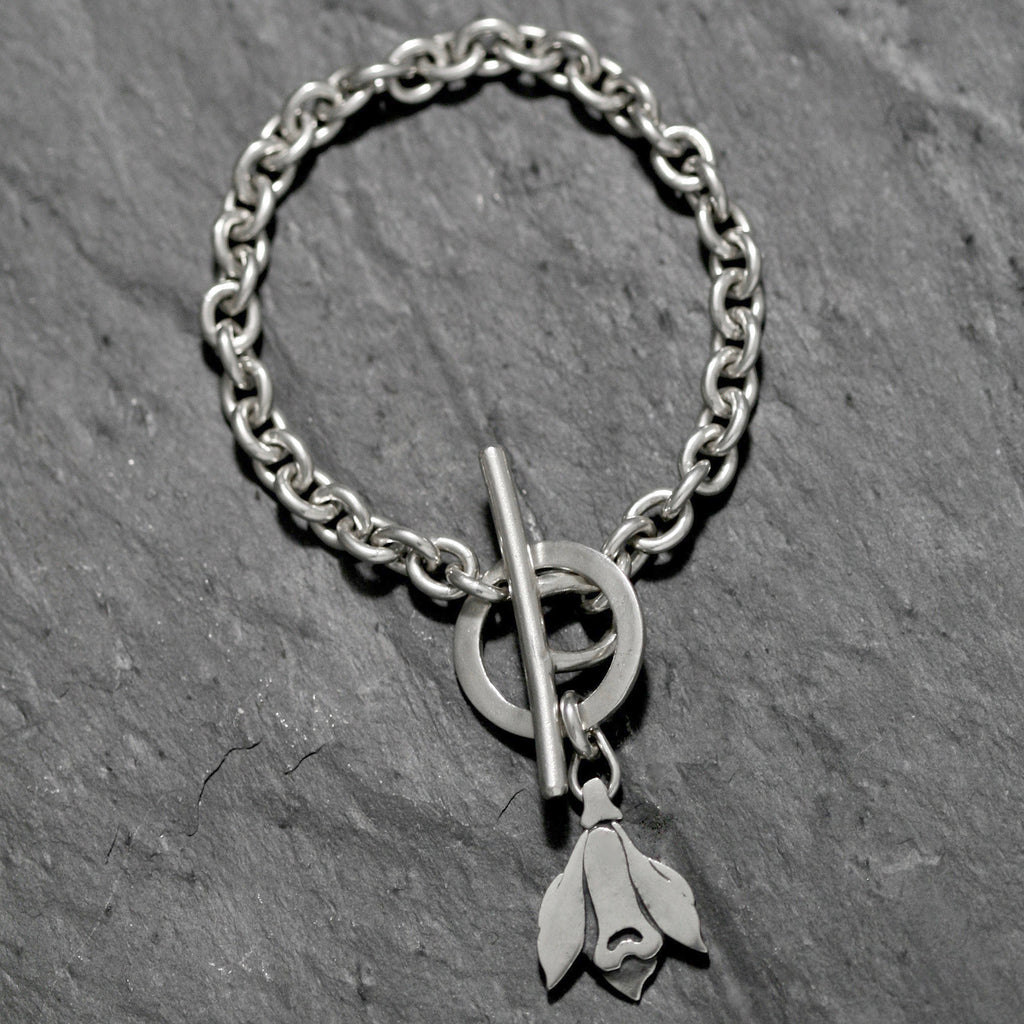 A simple Sterling silver flat snowdrop Art Deco floral design with a handmade catch. The heavy silver chain has a snowdrop charm hung from a small chain attached to the catch. Snowdrop flower bracelet made in Silver weighing 7 grams and on a stylish trace chain with a handmade T-bar catch.